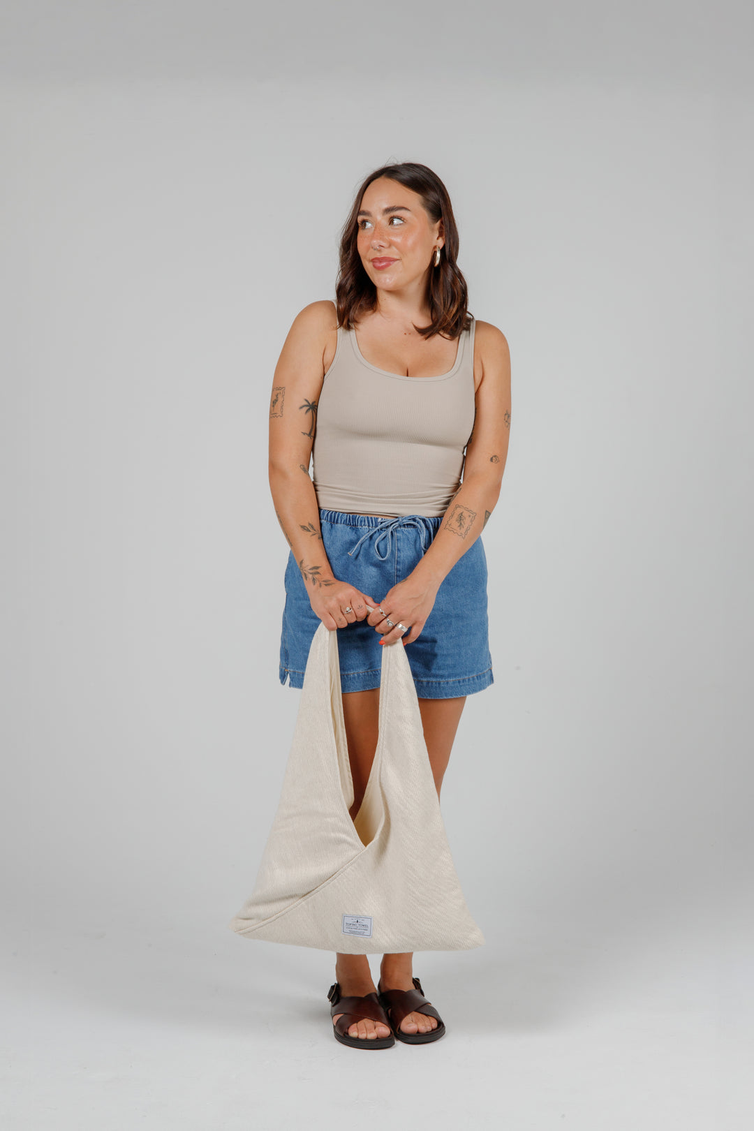 woman in jean shorts and a tank top holding a Slouchy white Turkish cotton hobo shoulder sling bag against a plain grey background