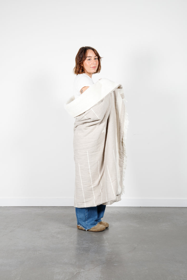 woman wrapped in a beige fleece lined throw with a minimal modern design in off white and eyelash fringe #colour_beige