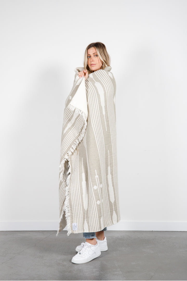 woman wrapped in a khaki and cream traditional geometric, fleece lined throw with eyelash fringe #colour_khaki