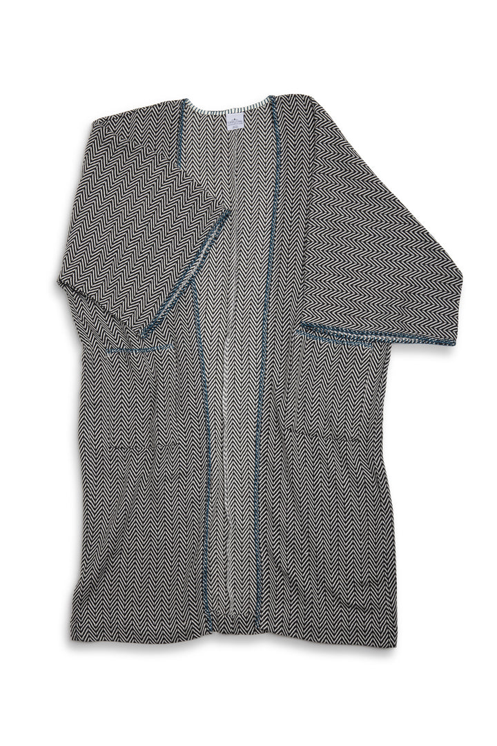 Long, herringbone patterned cardigan with blue whipstitch and pockets laid flat on a white background