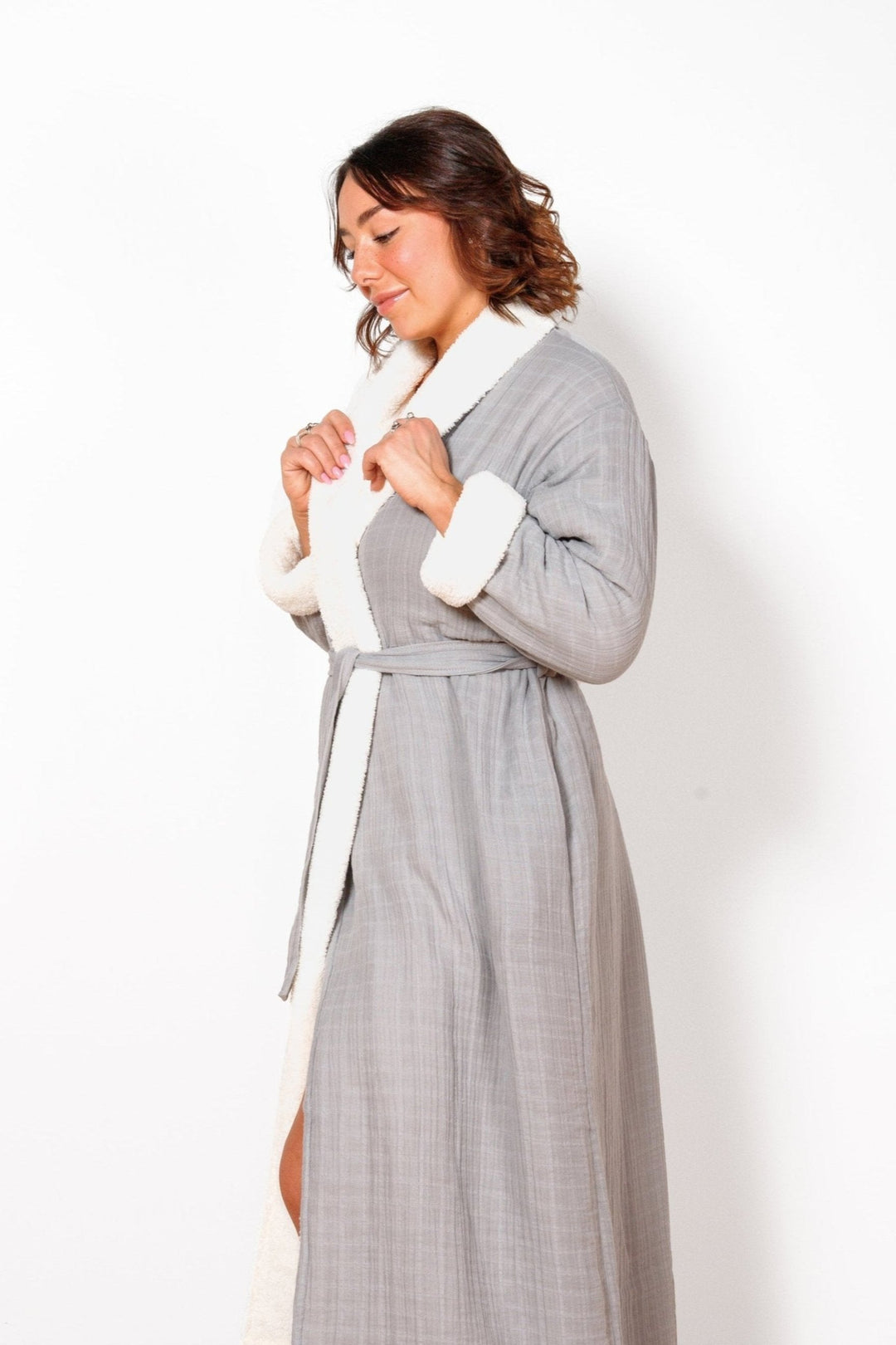 A woman wearing a long grey belted fleece lined muslin robe with pockets. #colour_grey
