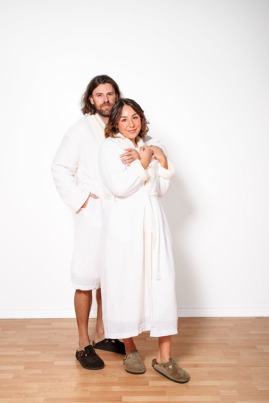 A man and  woman wearing long white belted fleece lined muslin robes with pockets. #colour_white