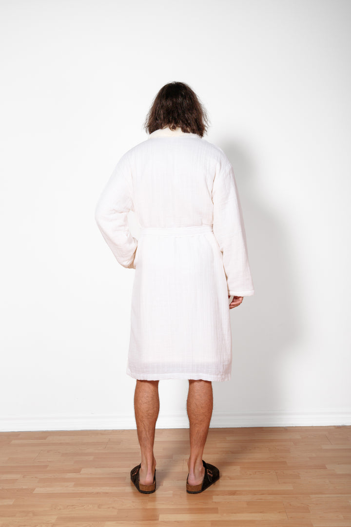 a man standing backwards wearing long white belted fleece lined muslin robe with pockets. #colour_white
