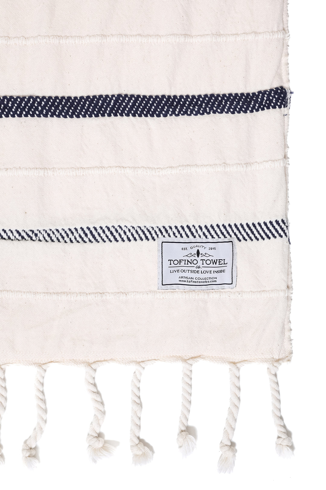 close up of an off white fleece lined throw with different shades of navy stripes and tassels 