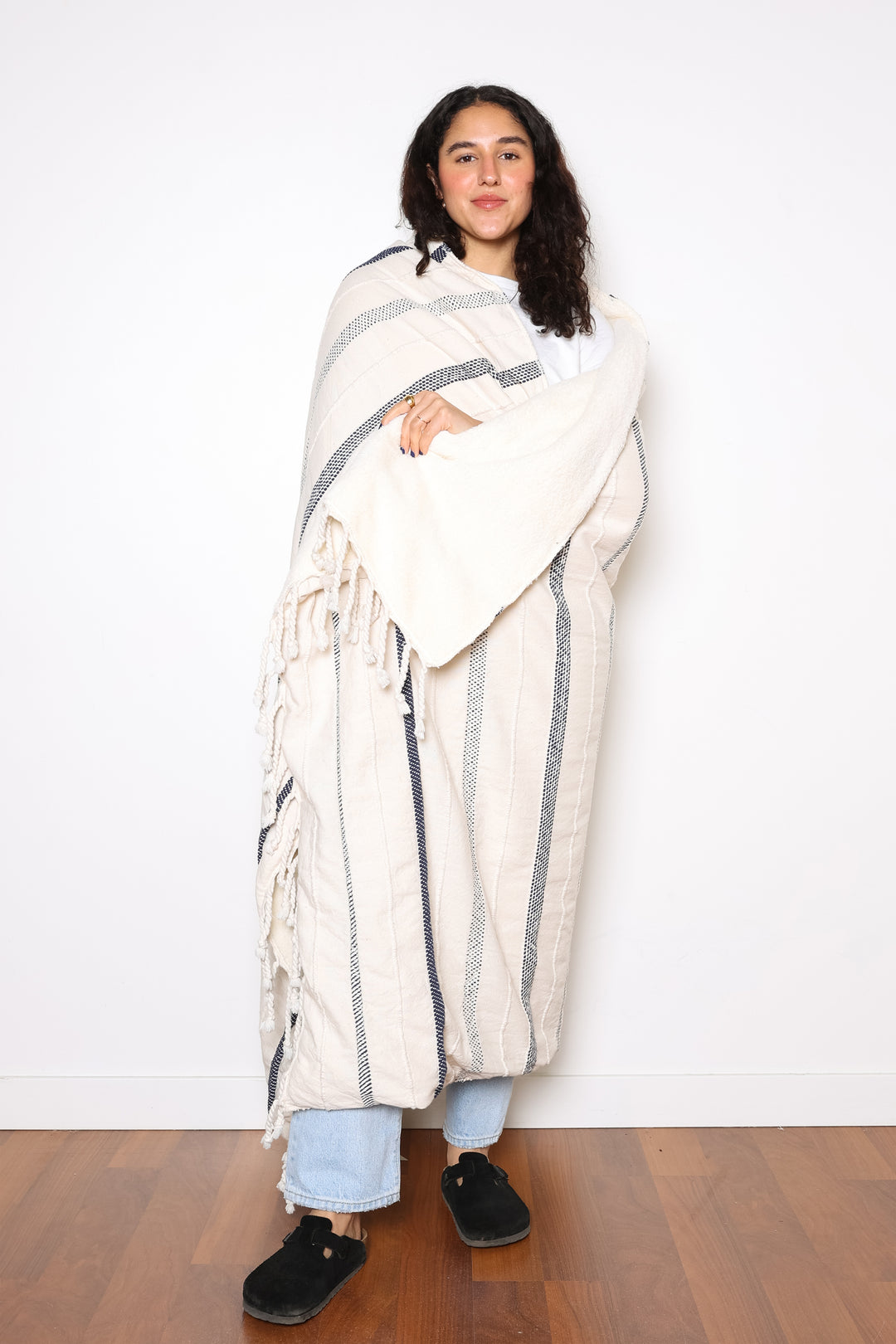 a women wrapped in an off white fleece lined throw with different shades of navy stripes and tassels