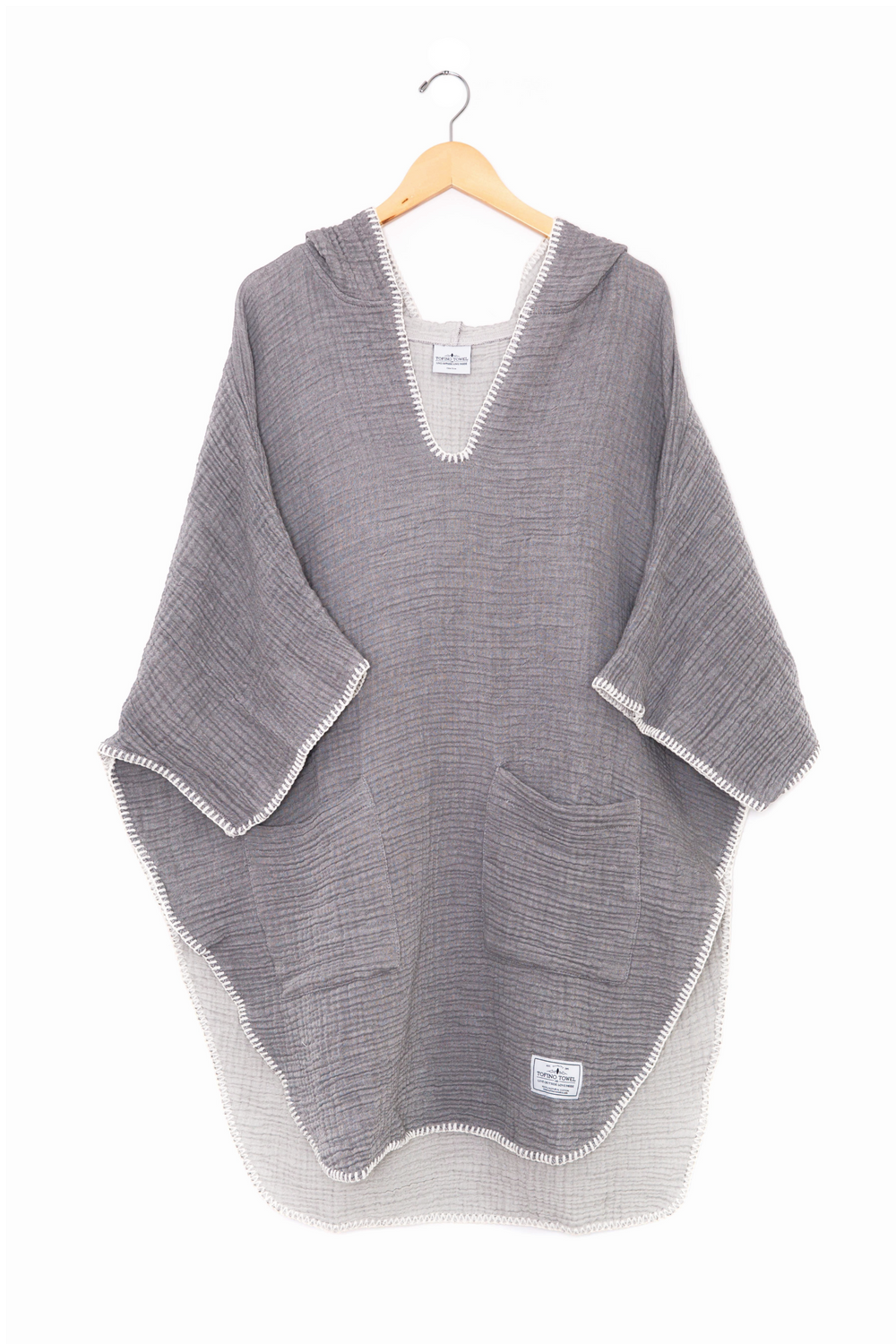 Dark grey muslin poncho with curved hem and oversized hood and front pockets  on a wooden hanger against a white background #colour_grey