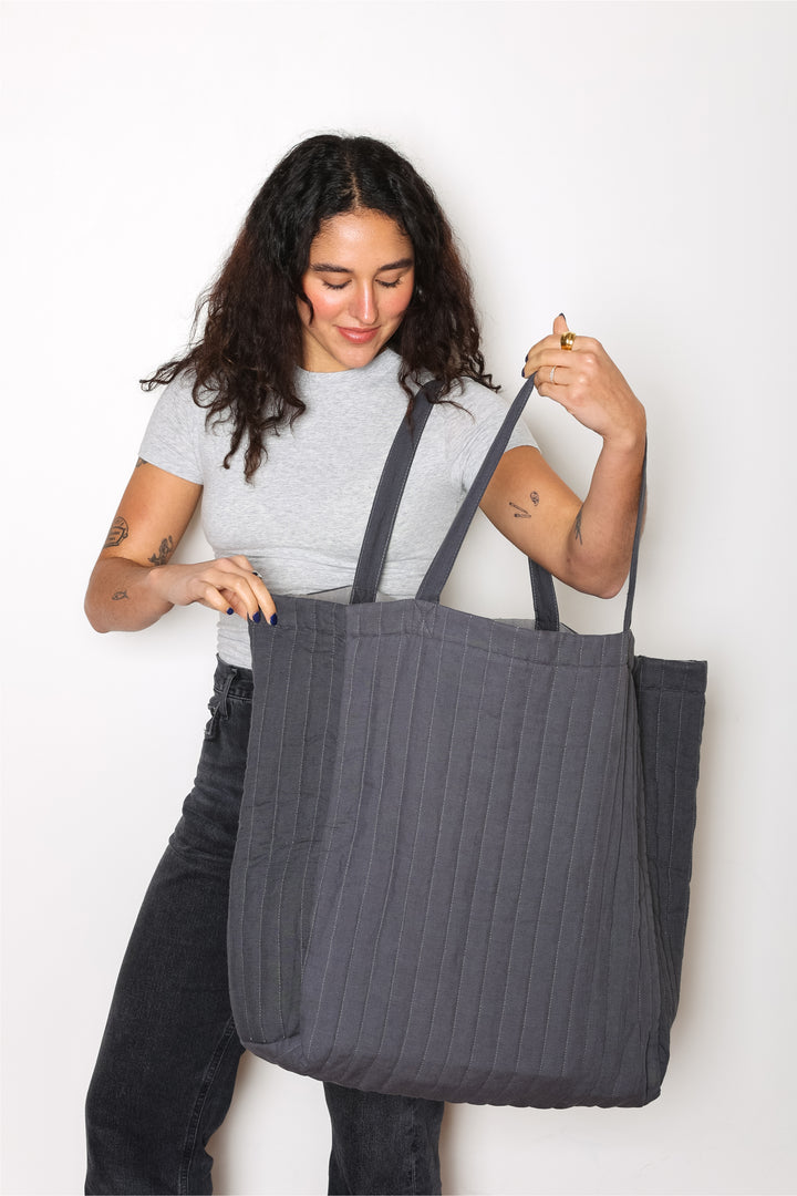 woman holding a An oversized quilted grey tote bag with zipper closure and shoulder straps.