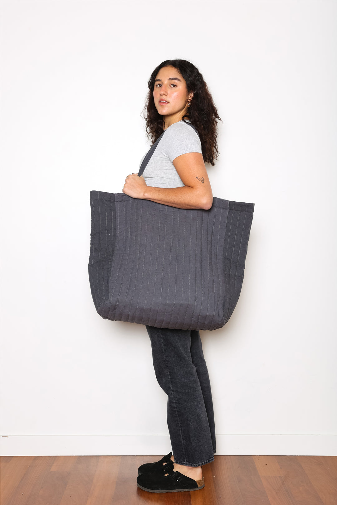 woman holding An oversized quilted grey tote bag with zipper closure and shoulder straps.