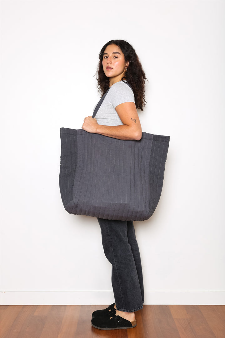 woman holding An oversized quilted grey tote bag with zipper closure and shoulder straps.