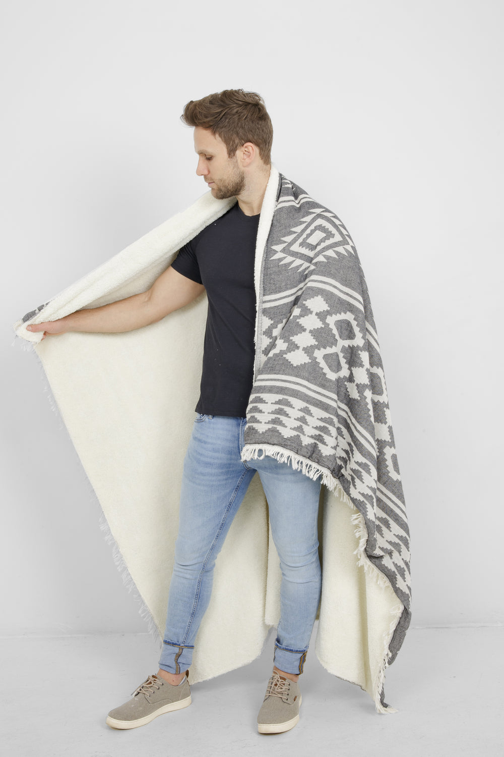 model wrapped up a dark grey and white patterned blanket with eyelash fringe and fleece lining #colour_granite