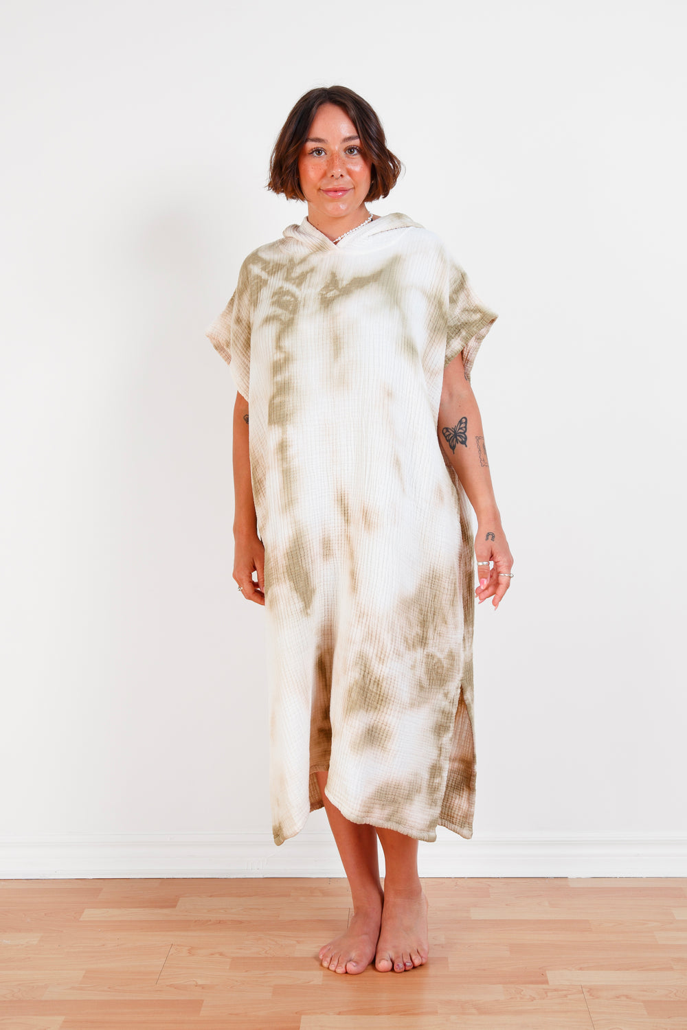 A woman standing wearing a white and beige khaki hooded, tie-dye muslin surf poncho with side slits  #colour_khaki-tie-dye