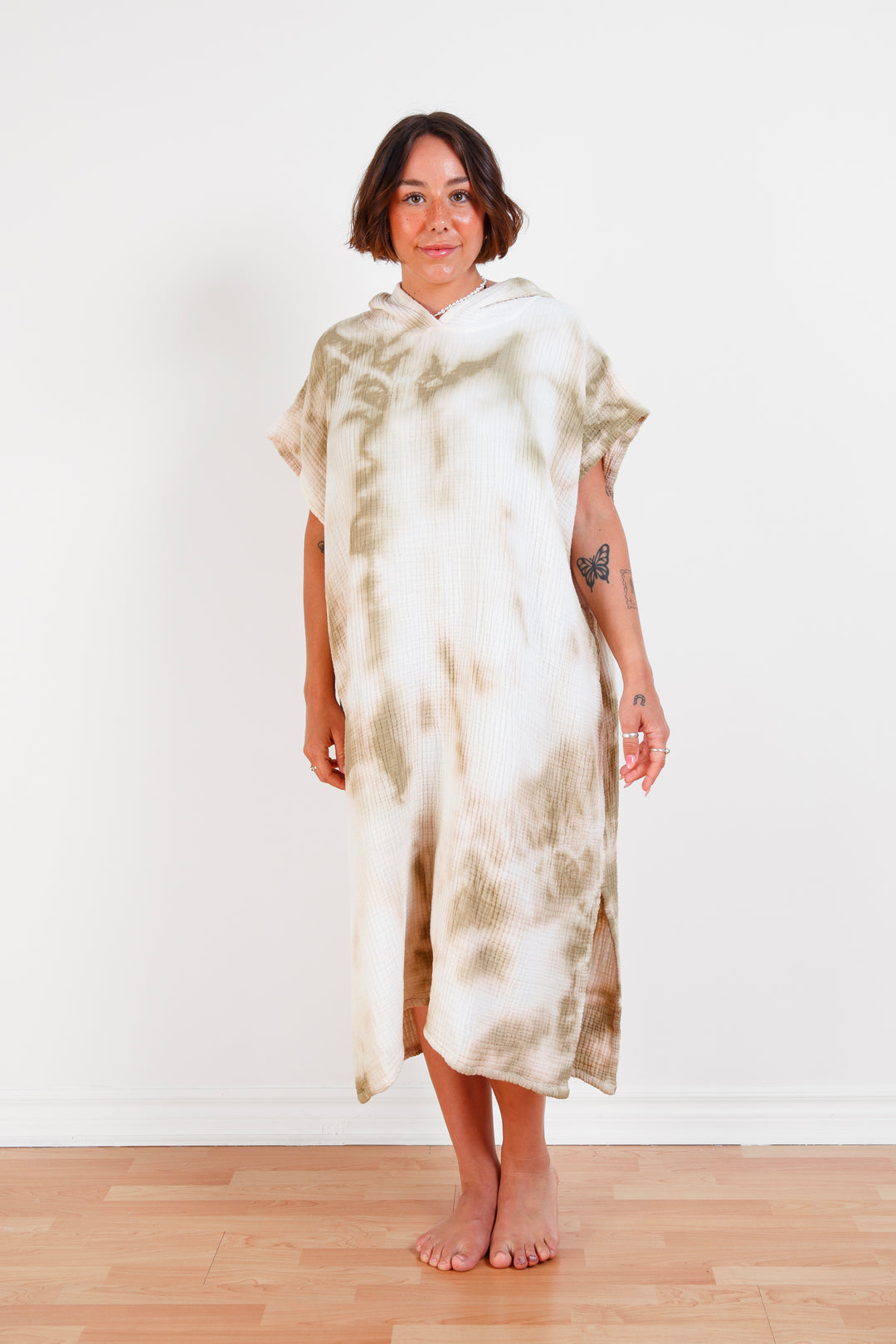 A woman standing wearing a white and beige khaki hooded, tie-dye muslin surf poncho with side slits  #colour_khaki-tie-dye