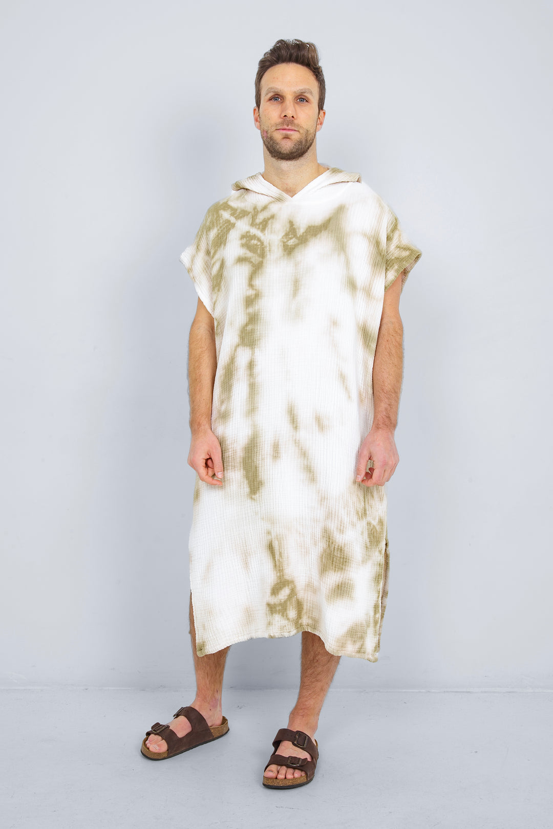 A man standing wearing a white and beige khaki hooded, tie-dye muslin surf poncho with side slits  #colour_khaki-tie-dye
