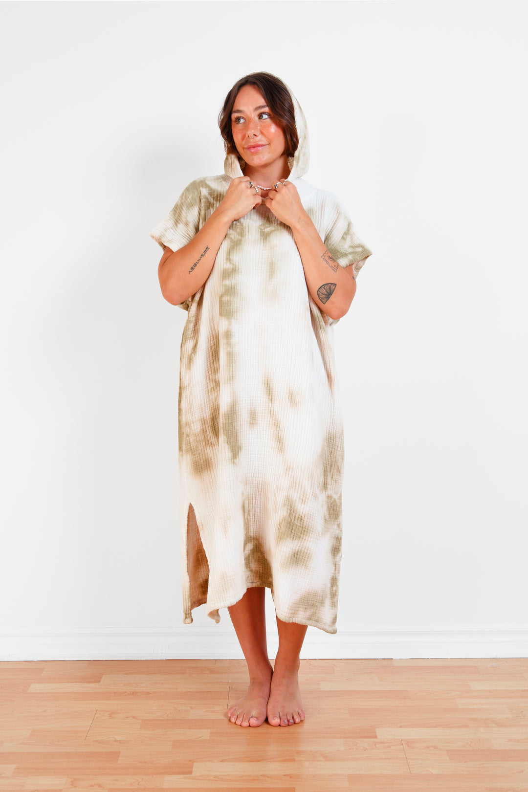 A woman standing wearing a white and beige khaki hooded, tie-dye muslin surf poncho with side slits  #colour_khaki-tie-dye