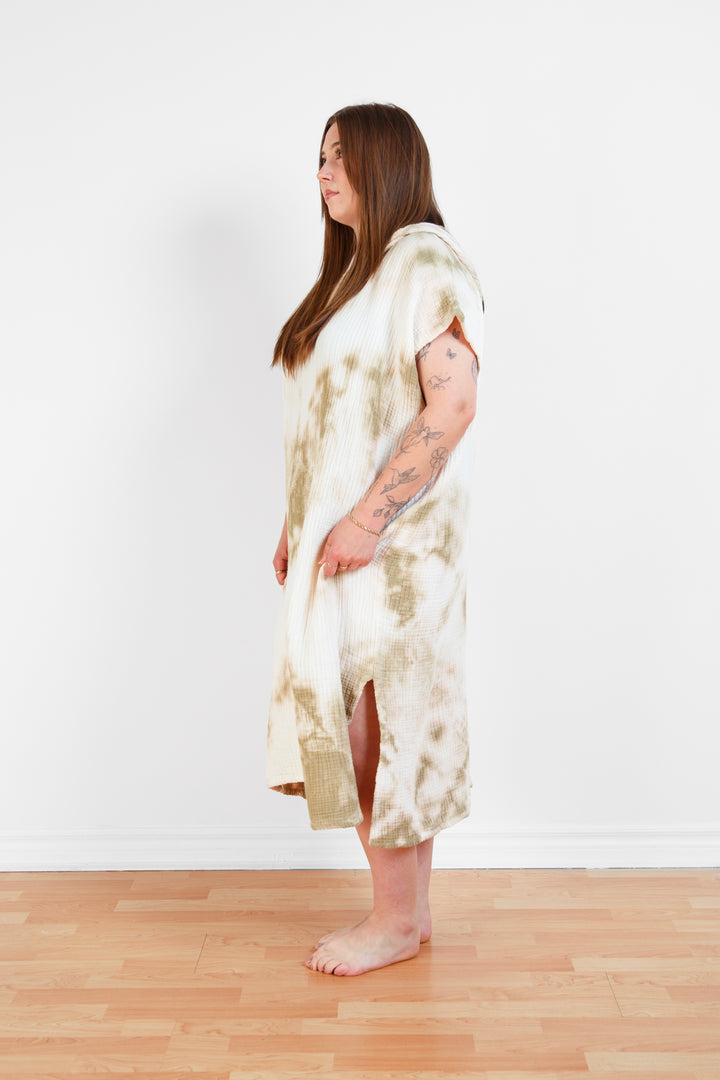 A woman standing wearing a white and beige khaki hooded, tie-dye muslin surf poncho with side slits  #colour_khaki-tie-dye