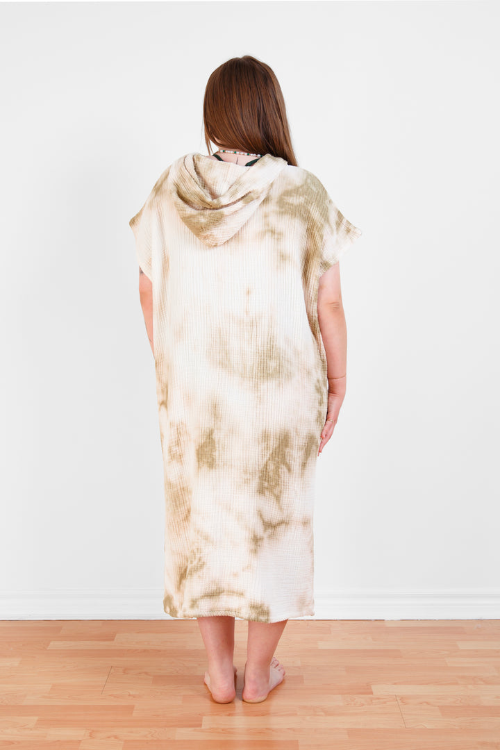 A woman standing backwards wearing a white and beige khaki hooded, tie-dye muslin surf poncho with side slits  #colour_khaki-tie-dye
