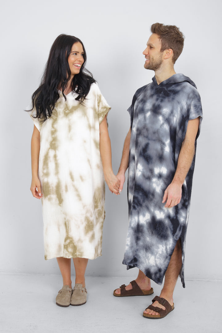 A man and a woman standing side by side wearing hooded, tie-dye muslin surf ponchos with side slits in different colors.  #colour_khaki-tie-dye