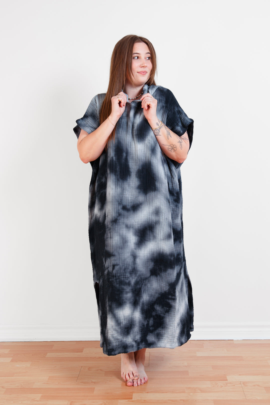 A woman standing wearing a dark blue and white hooded, tie-dye muslin surf poncho with side slits  #colour_ocean-tie-dye