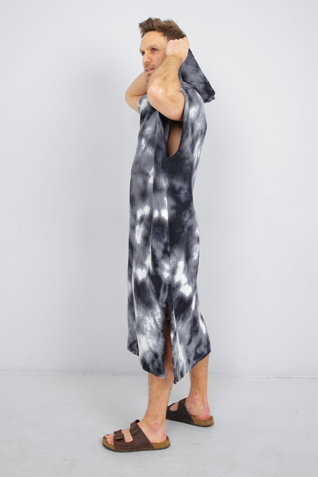 A man standing wearing a dark blue and white hooded, tie-dye muslin surf poncho with side slits  #colour_ocean-tie-dye