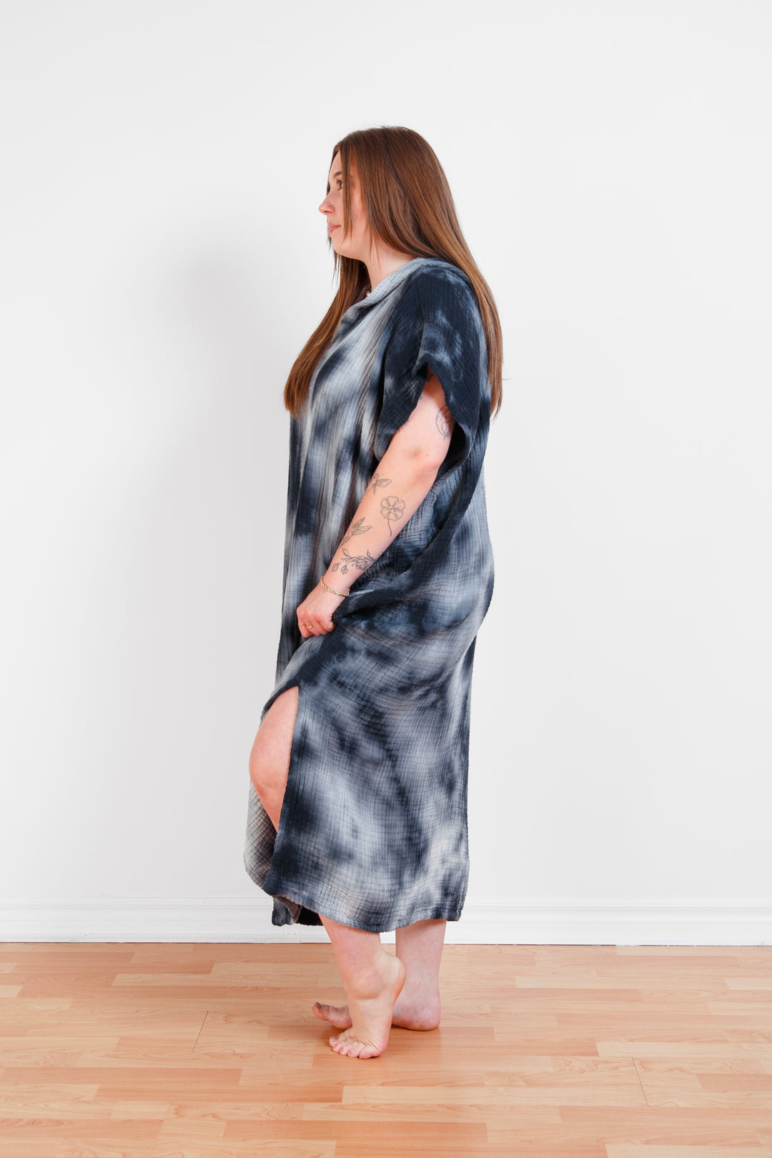 A woman standing wearing a dark blue and white hooded, tie-dye muslin surf poncho with side slits  #colour_ocean-tie-dye
