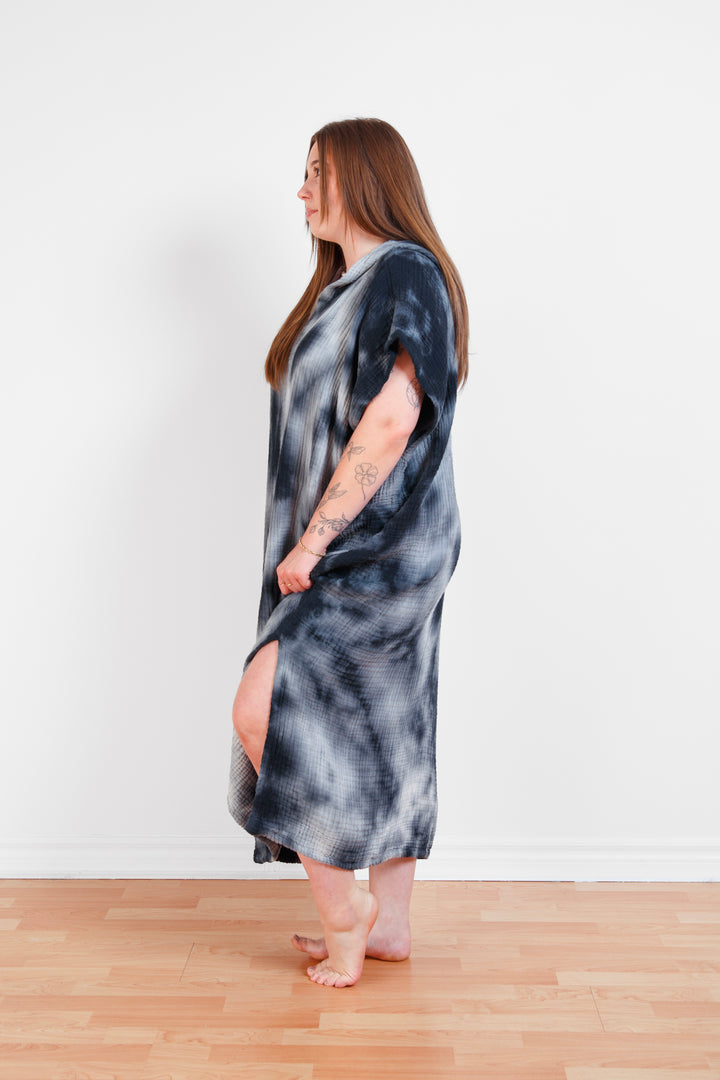 A woman standing wearing a dark blue and white hooded, tie-dye muslin surf poncho with side slits  #colour_ocean-tie-dye