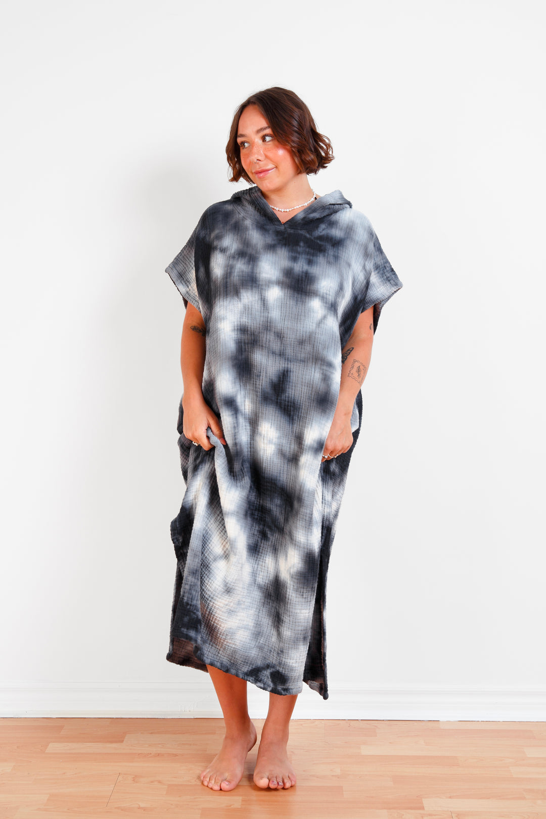 A woman standing wearing a dark blue and white hooded, tie-dye muslin surf poncho with side slits  #colour_ocean-tie-dye