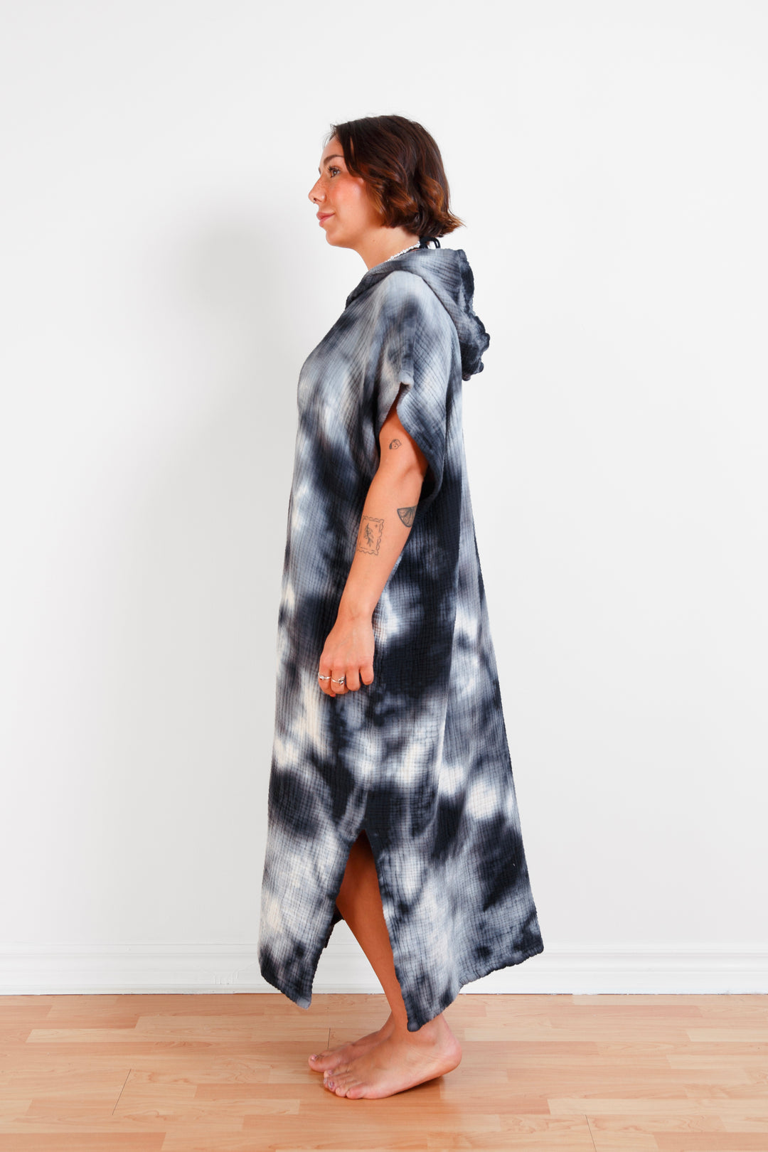 A woman standing wearing a dark blue and white hooded, tie-dye muslin surf poncho with side slits  #colour_ocean-tie-dye