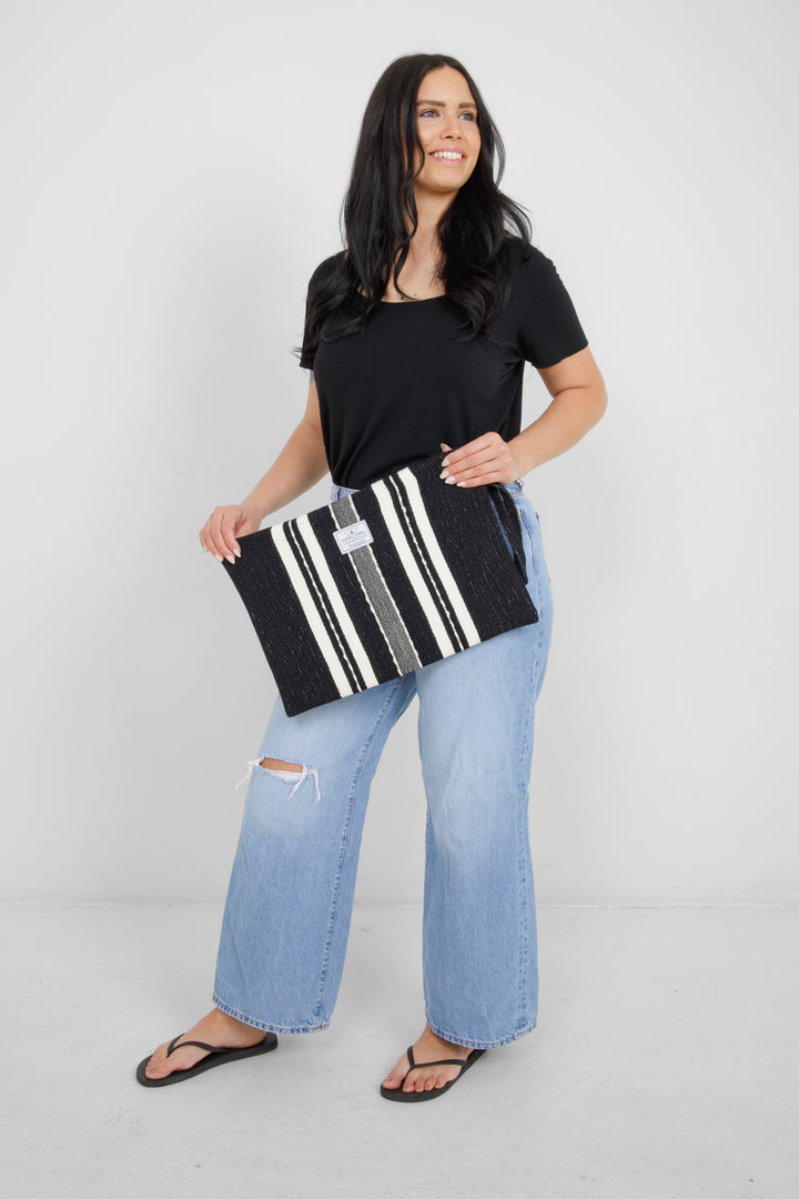 Woman holding in light blue jeans and a black t shirt holding a Large black zip up pouch with white stripes and a wrist handle on a white background