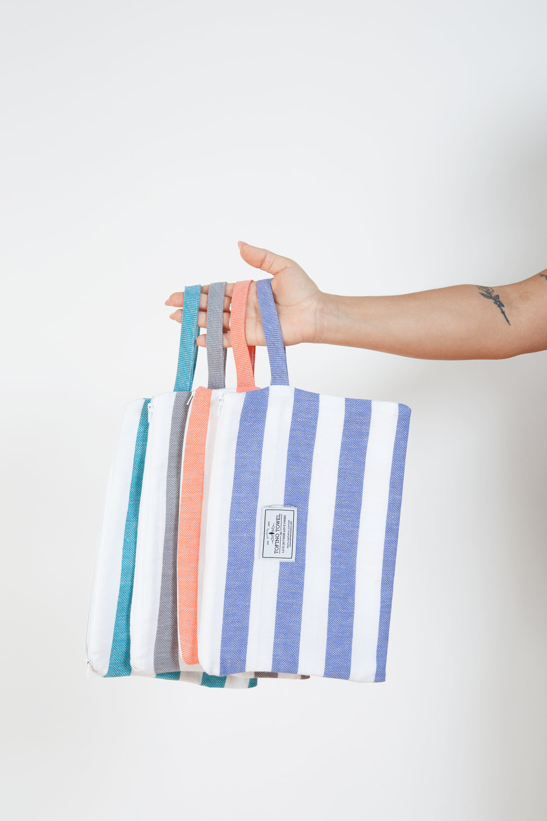 woman holding four different coloured striped zipped pouches with wrist straps#colour_grey-stripes