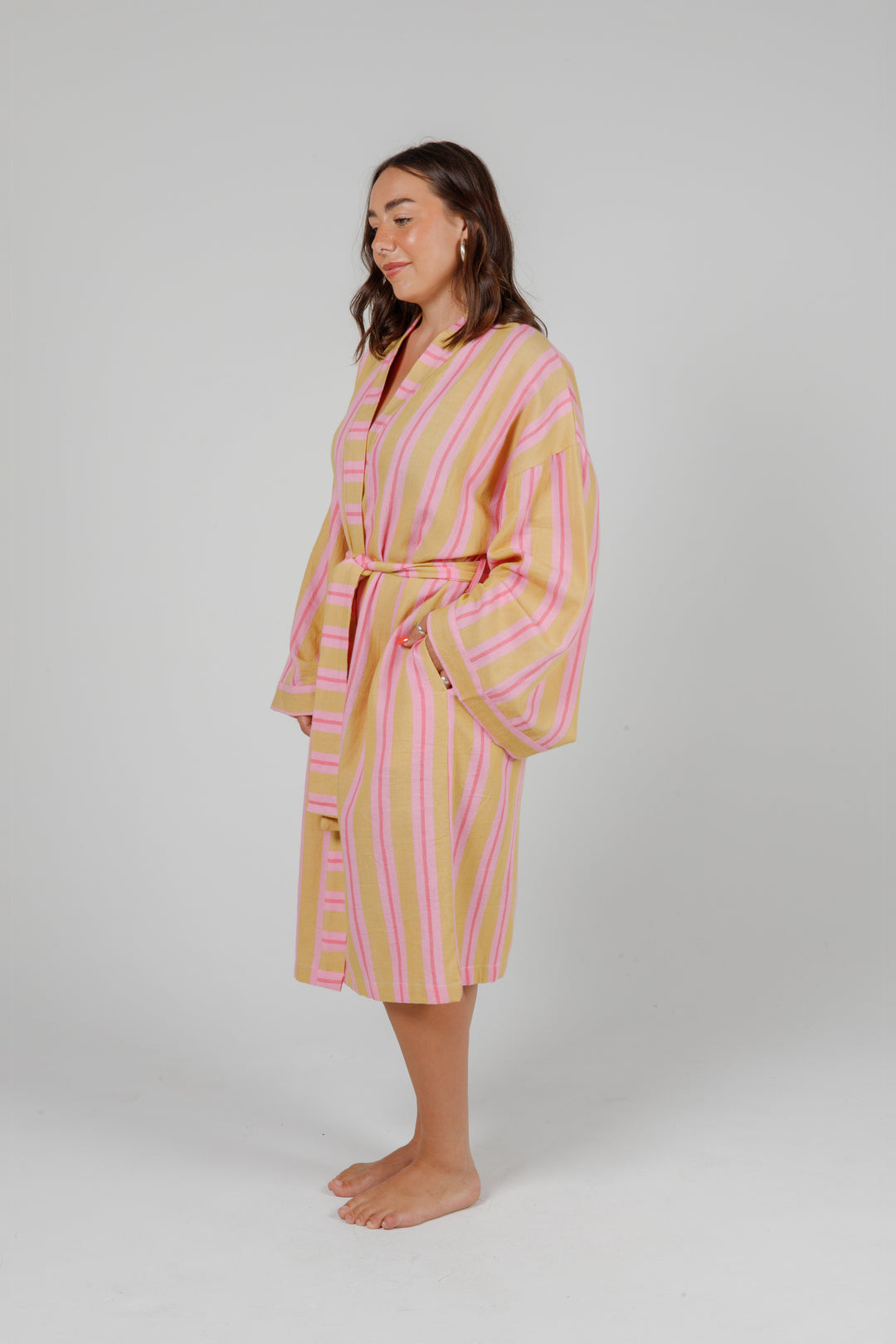 women wearing a light orange robe with light and dark pink stripes standing in front of a plain light grey background #colour_sunset-mix