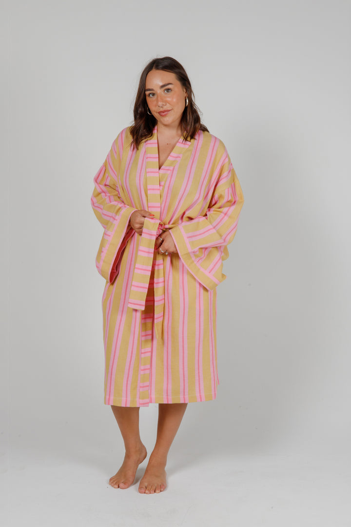women wearing a light orange robe with light and dark pink stripes standing in front of a plain light grey background #colour_sunset-mix