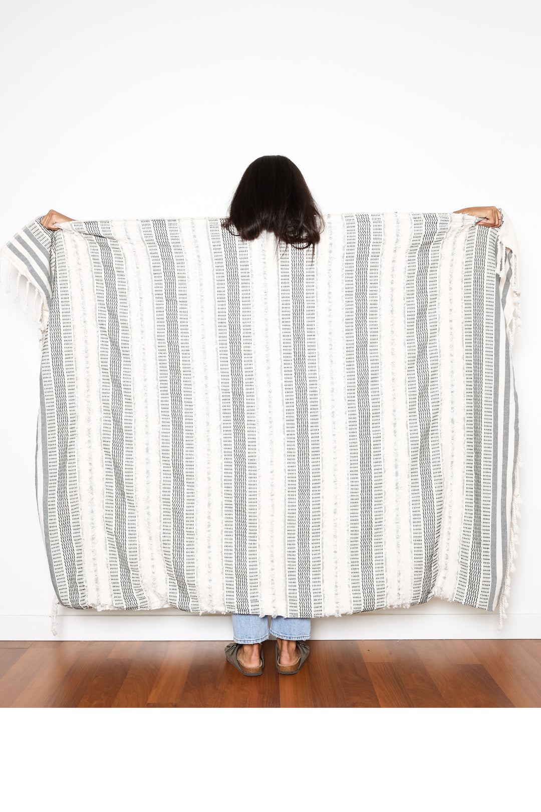 women standing backwards holding out a cream and black fleece lined throw with textured stripes and tassels behind her  #colour_black-stripe