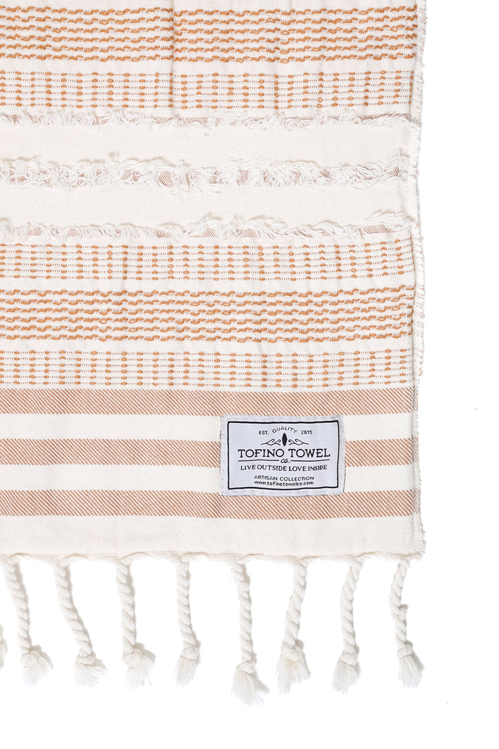 close up of cream and light brown fleece lined throw with textured stripes and tassels on a white background #colour_camel-stripe