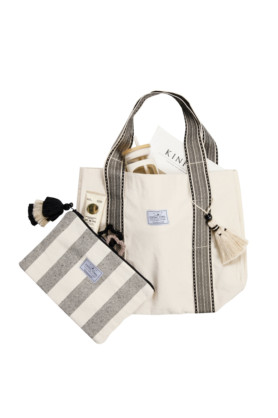 A speckled grey and off white striped canvas toiletry bag / pouch / clutch with a tasseled zipper in front of a coordinating tote bag against a plain background