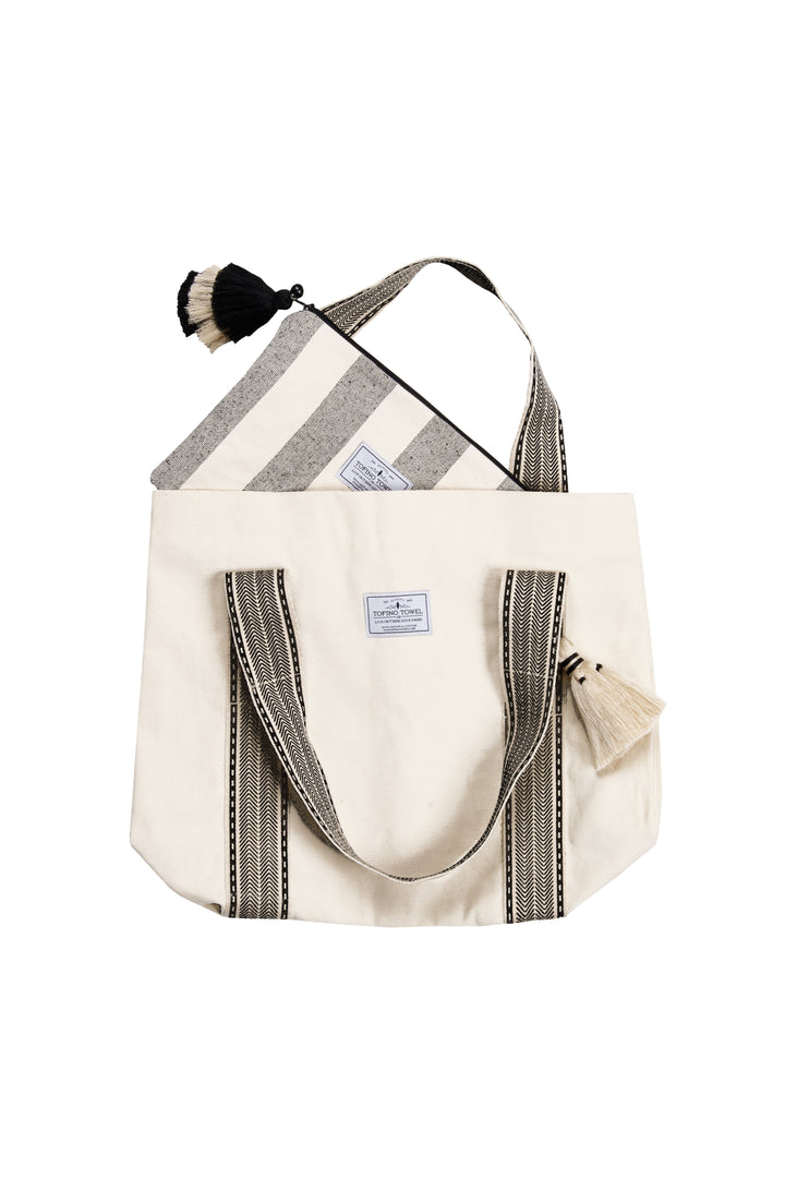 A speckled grey and off white striped canvas toiletry bag / pouch / clutch with a tasseled zipper inside of a coordinating tote bag against a plain background