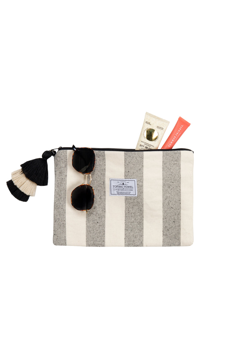 speckled grey and off white striped canvas toiletry bag pouch with a tasseled zipper holding accessories on a white background