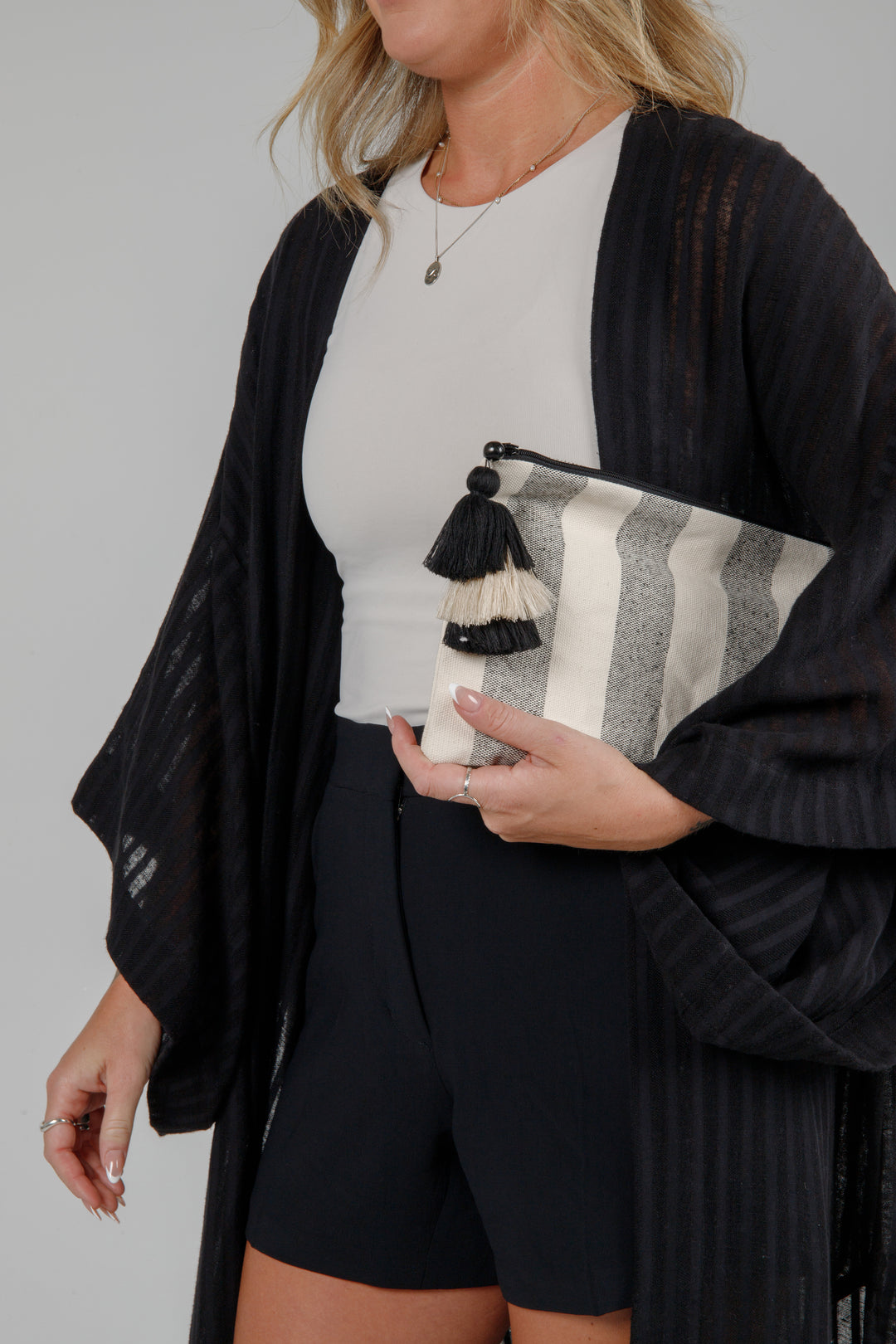 Person holding a speckled grey and off white striped canvas toiletry bag / pouch / clutch with a tasseled zipper against a plain background