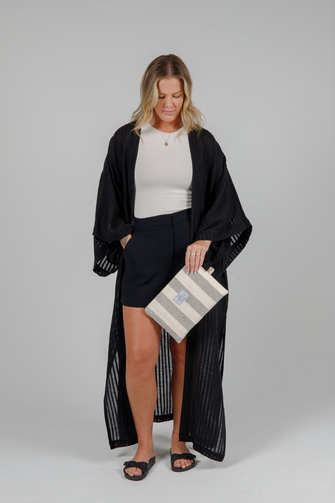 Person holding a speckled grey and off white striped canvas toiletry bag / pouch / clutch with a tasseled zipper against a plain background