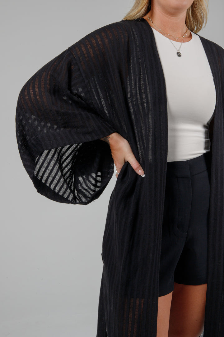 close up of sleeve and fabric Long black semi-sheer linen blend cover-up with wide kimono sleeves and side slits, full-length lightweight beach kimono layered over neutral outfit for resort wear style