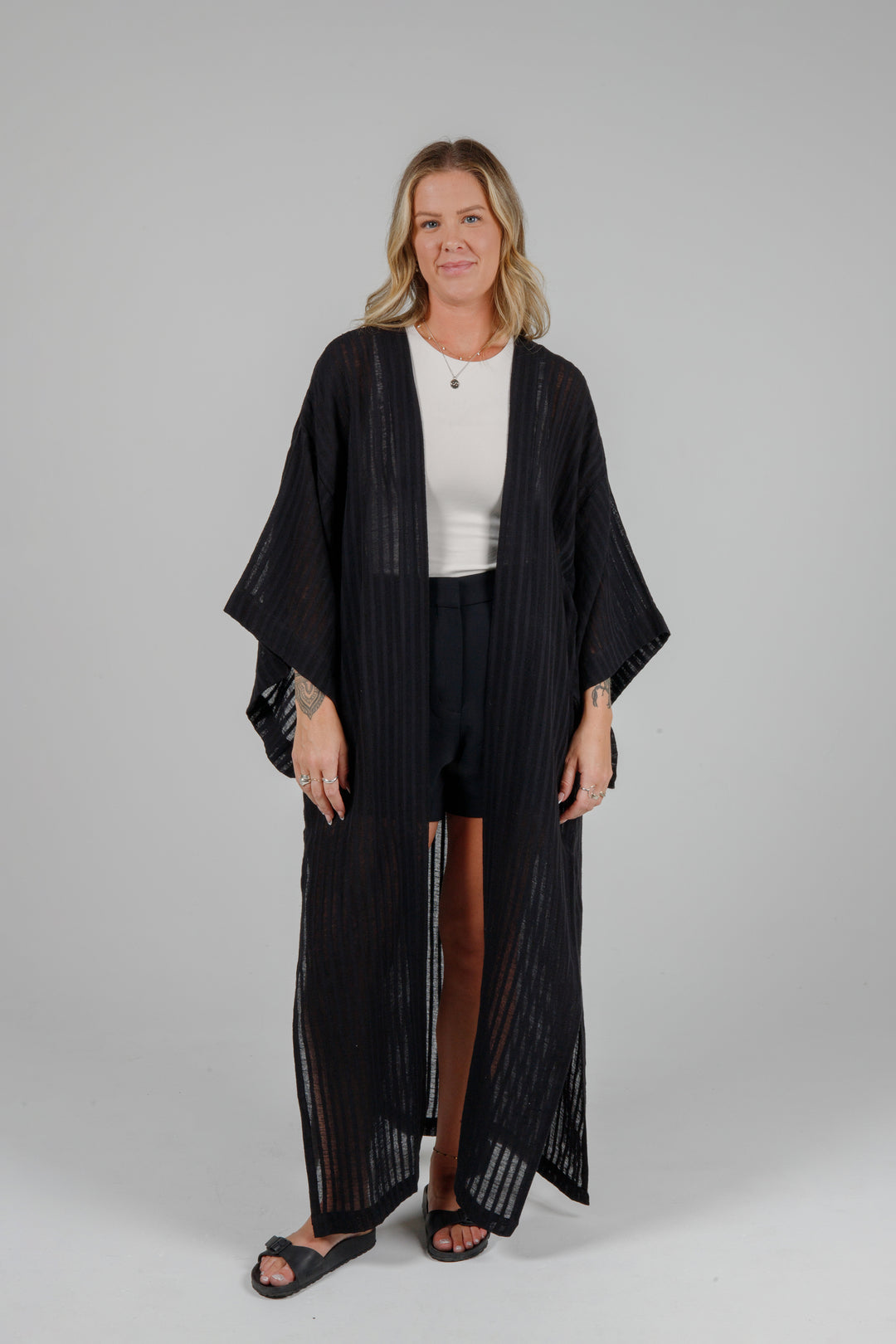 full front relaxed view of Long black semi-sheer linen blend cover-up with wide kimono sleeves and side slits, full-length lightweight beach kimono layered over neutral outfit for resort wear style