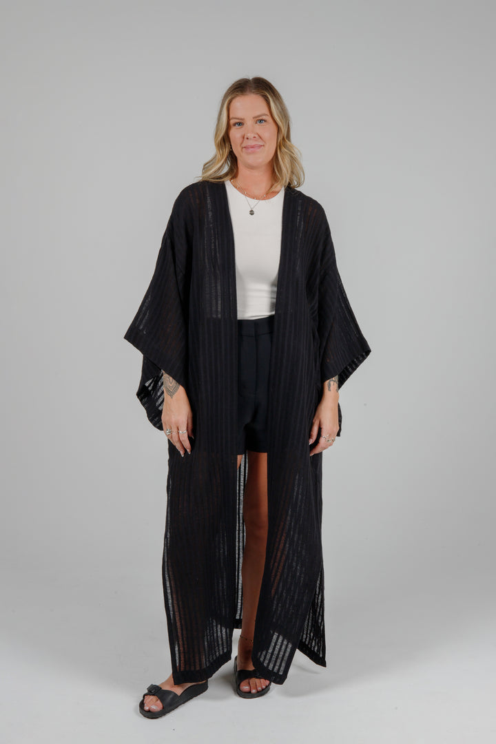 full front relaxed view of Long black semi-sheer linen blend cover-up with wide kimono sleeves and side slits, full-length lightweight beach kimono layered over neutral outfit for resort wear style