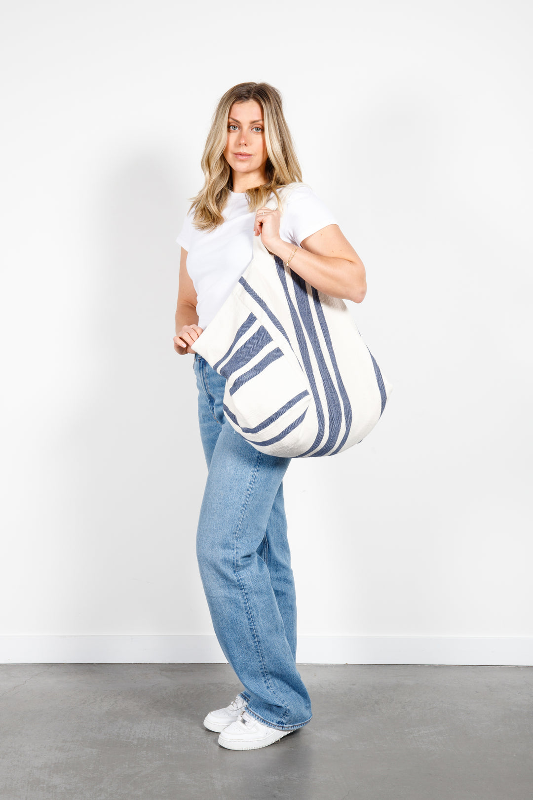 model in white tank top and blue jeans wearing oversized white and blue striped Turkish cotton tote bag on a white background #colour_navy