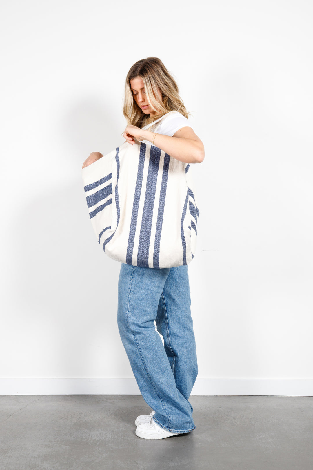model in white tank top and blue jeans wearing oversized white and blue striped Turkish cotton tote bag on a white background #colour_navy