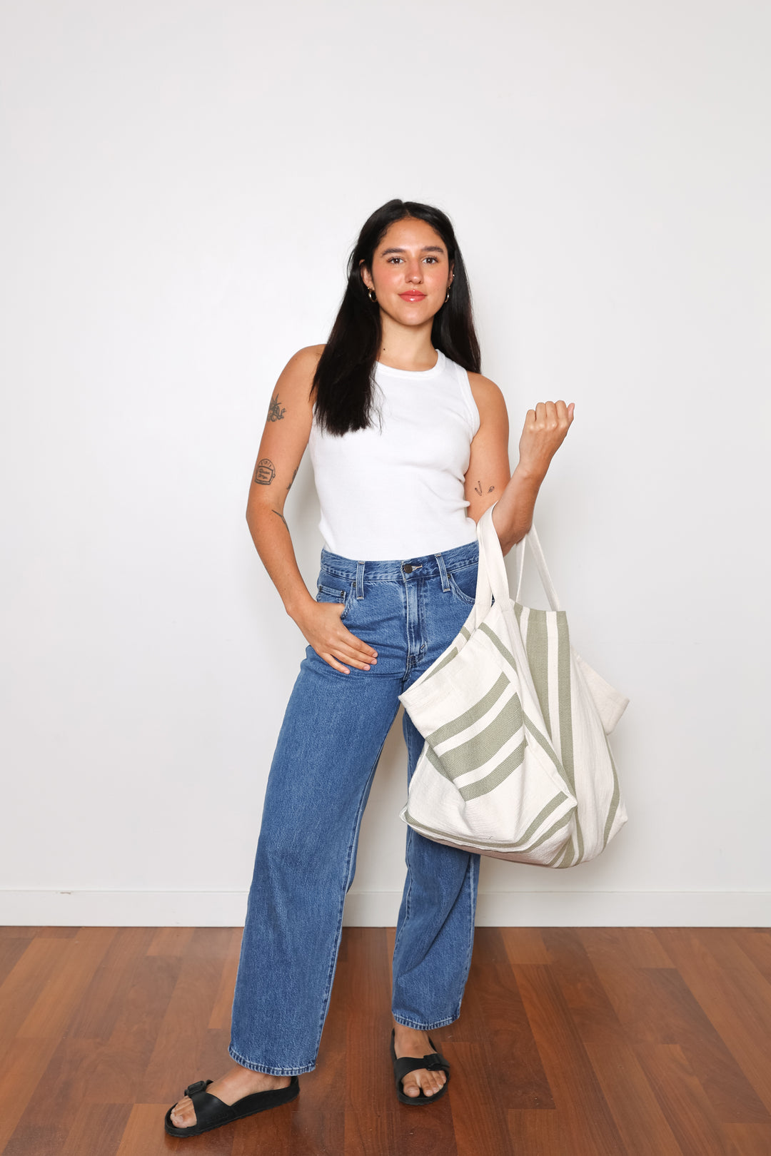 model in white tank top and blue jeans wearing oversized white and olive green striped Turkish cotton tote bag on a white background #colour_olive