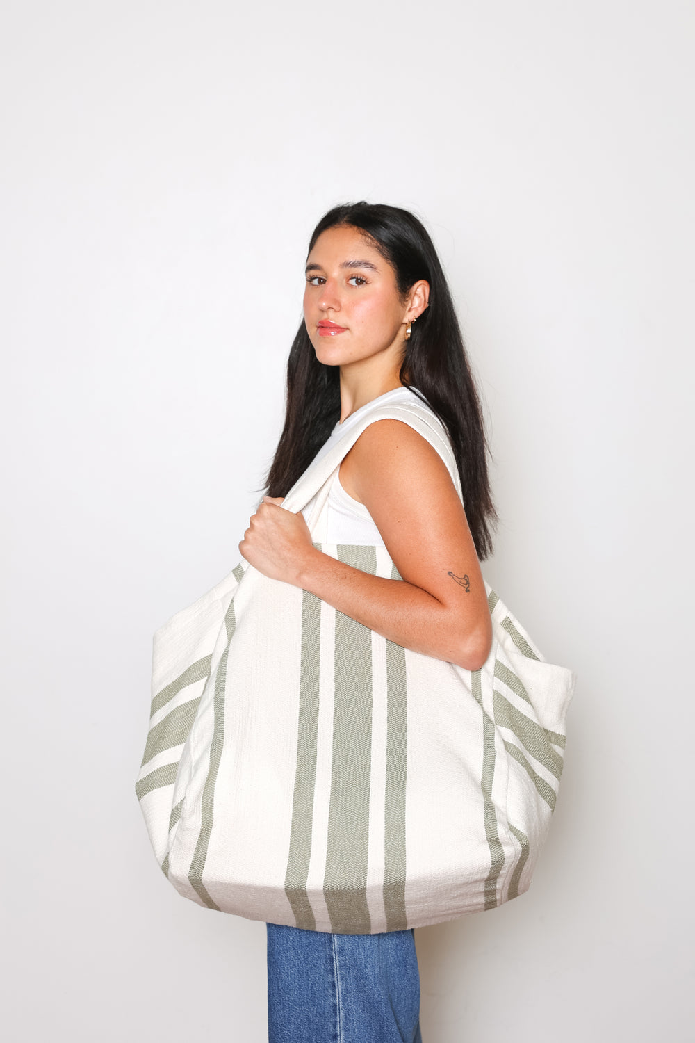 model in white tank top and blue jeans wearing oversized white and olive green striped Turkish cotton tote bag on a white background #colour_olive