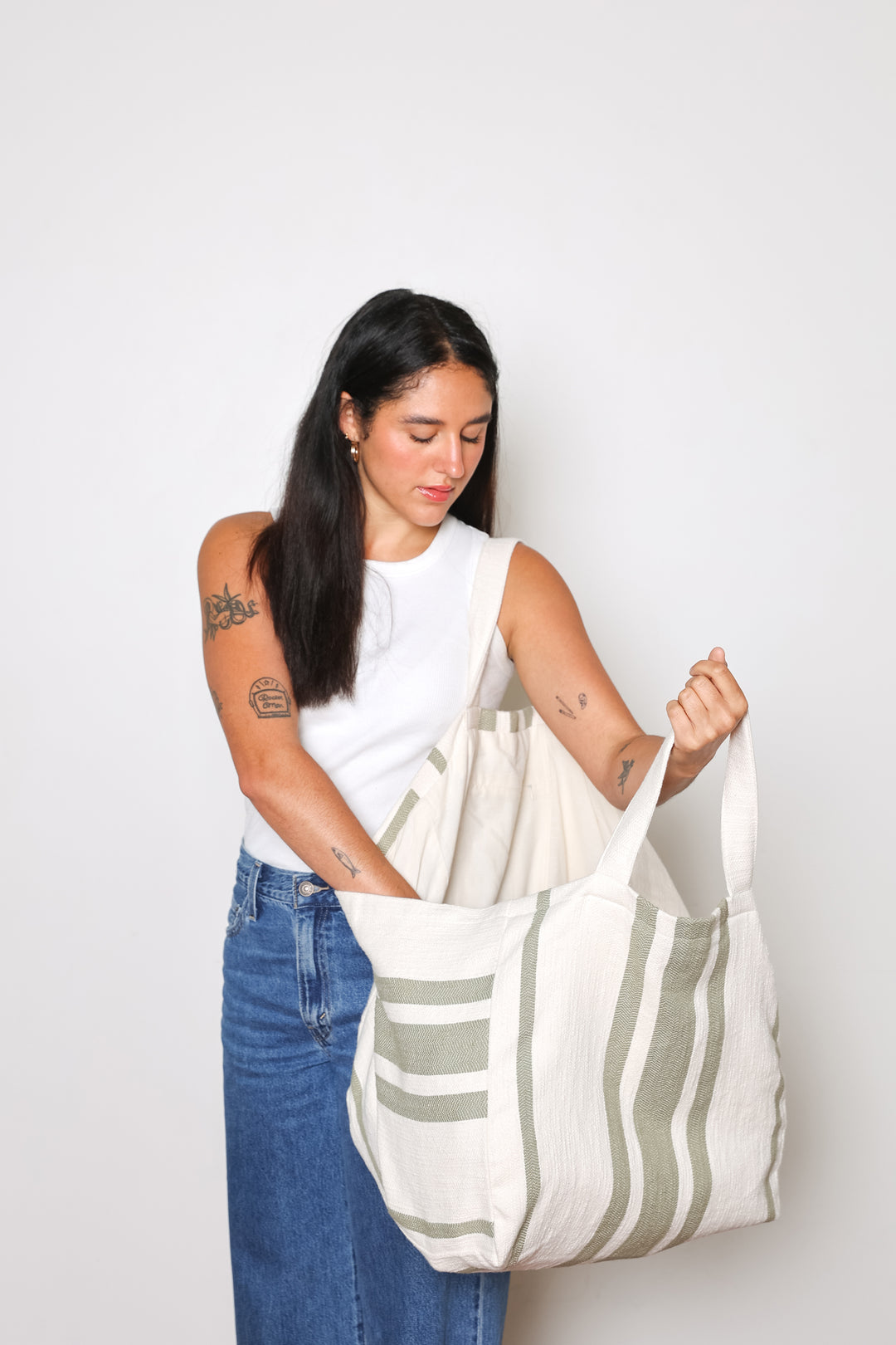 model in white tank top and blue jeans wearing oversized white and olive green striped Turkish cotton tote bag on a white background #colour_olive