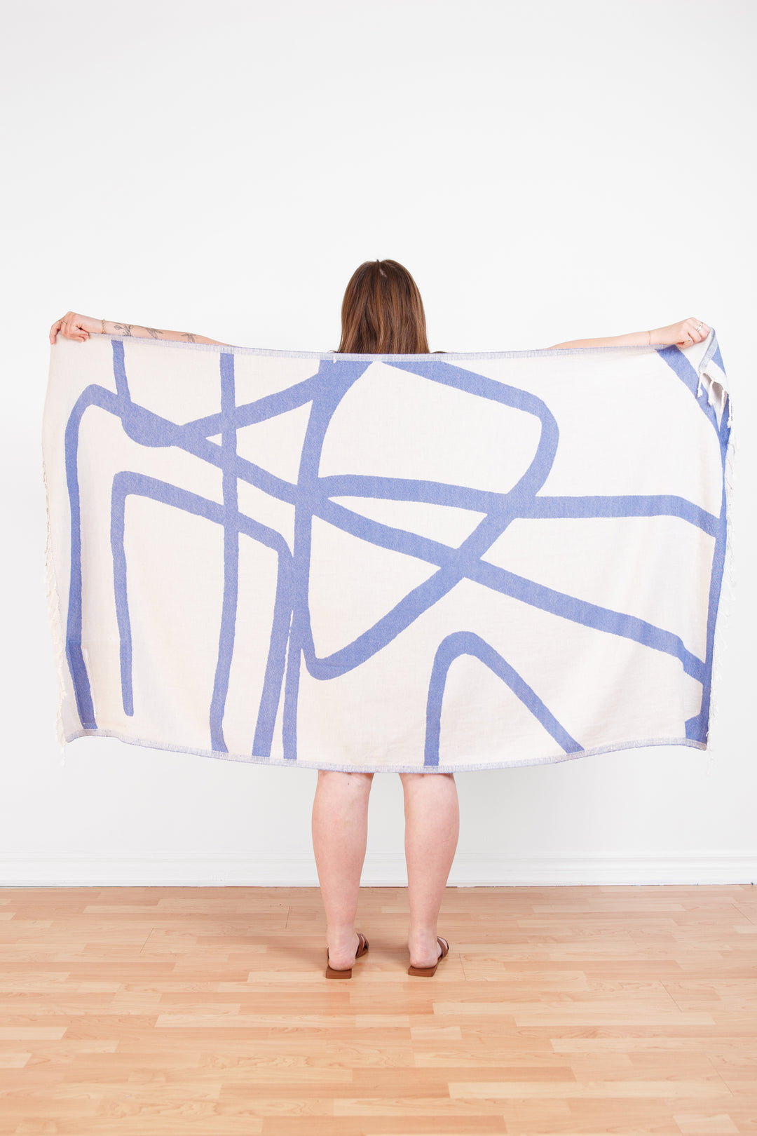 model holding up a Turkish cotton towel with an abstract white and blue design and eyelash fringe and on a white background #colour_blue