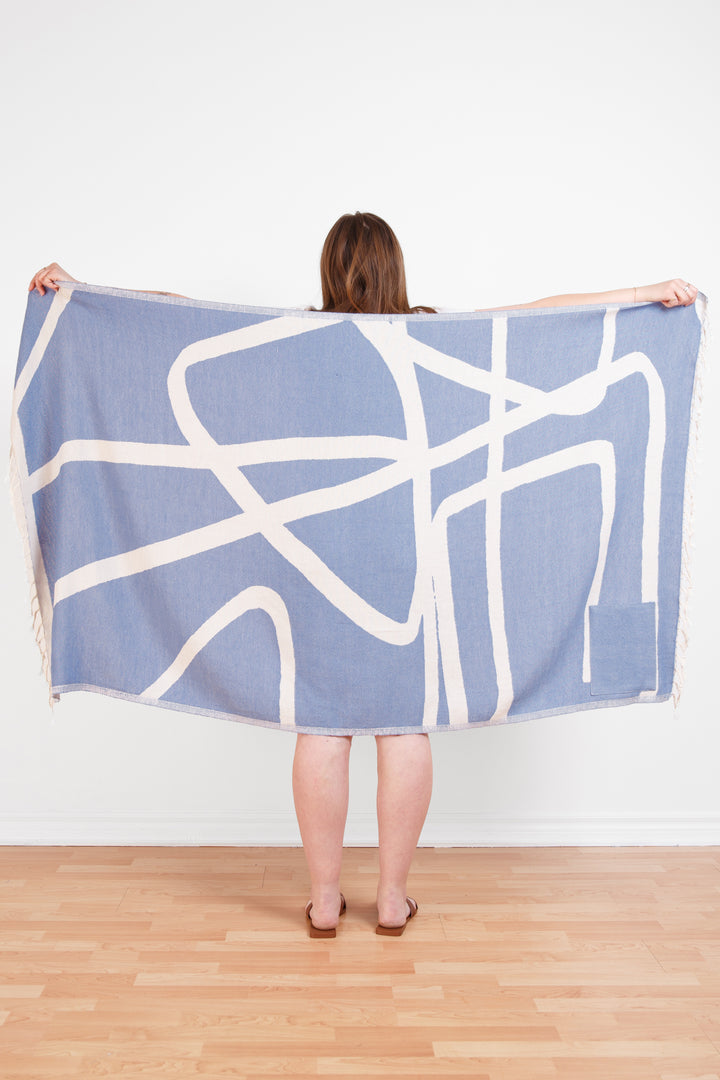 model holding up a Turkish cotton towel with an abstract white and blue design and eyelash fringe and on a white background #colour_blue