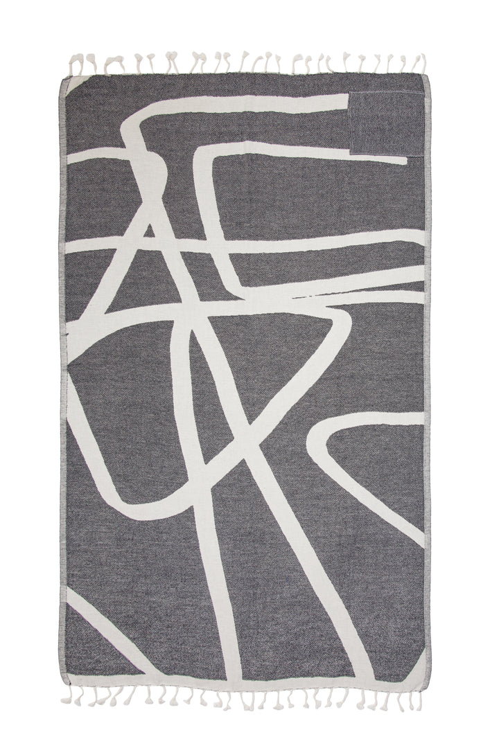 Turkish cotton towel with an abstract white and dark grey design, eyelash fringe and discreet zipper pocket laid flat on a white background #colour_granite