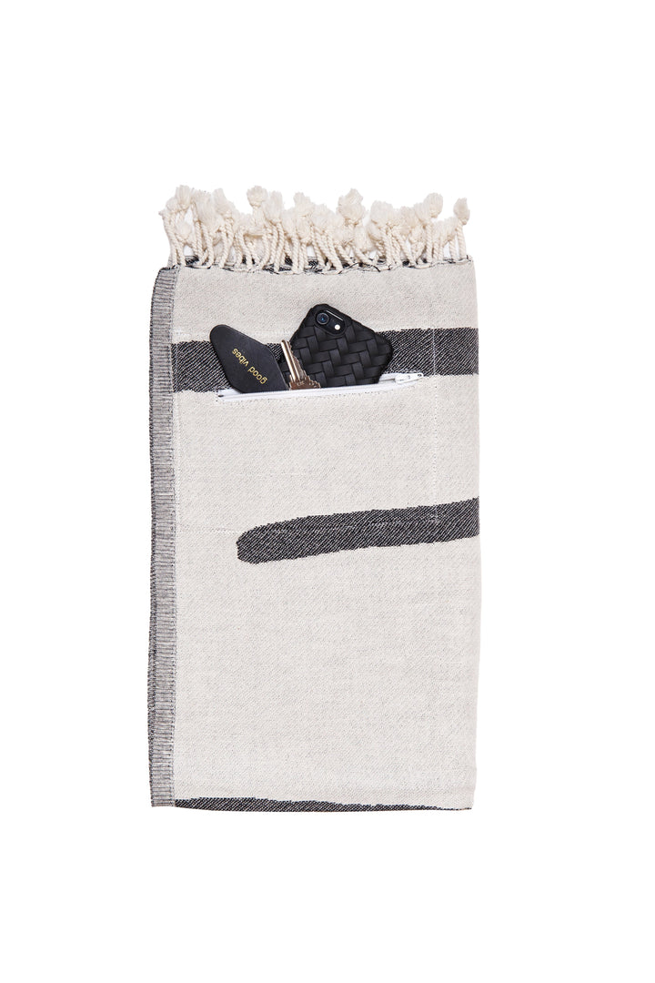 Turkish cotton towel with an abstract white and dark grey design, eyelash fringe and discreet zipper pocket laid folded on a white background #colour_granite